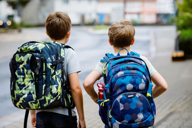 Two little kid boys with backpack or satchel. Schoolkids on the way to school. Healthy adorable children, brothers and