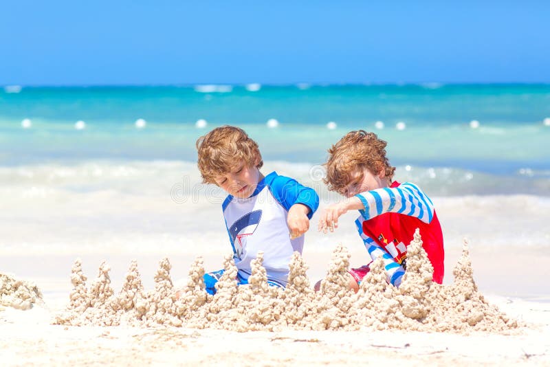 Two little kids boys having fun with building a sand castle on tropical beach on island. Healthy children playing