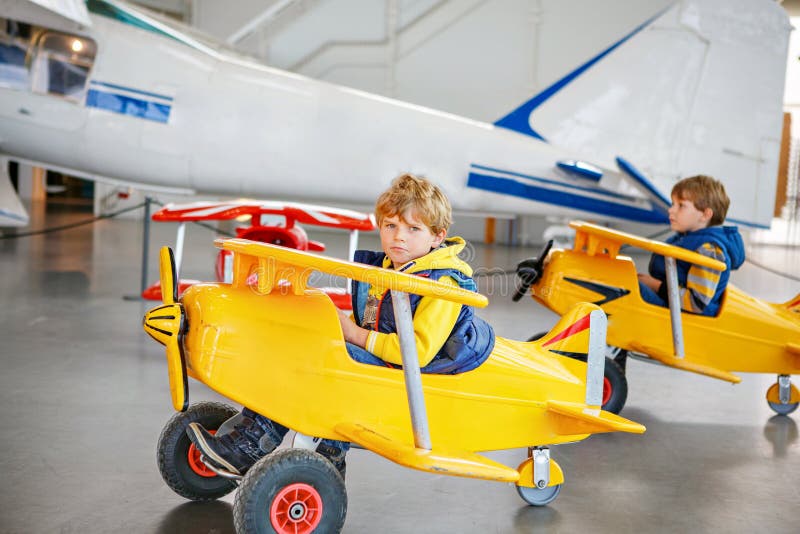 Two little kids boysy driving big toy old vintage pedal plane and having fun, indoors. Active leisure with children