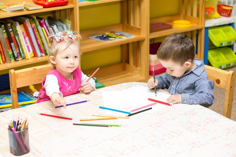 Two little kids drawing with colorful pencils in preschool at the table. Little girl and boy drawing