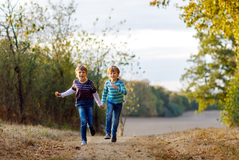 Two little school kids boys running and jumping in forest. Happy children, best friends and siblings having fun on warm