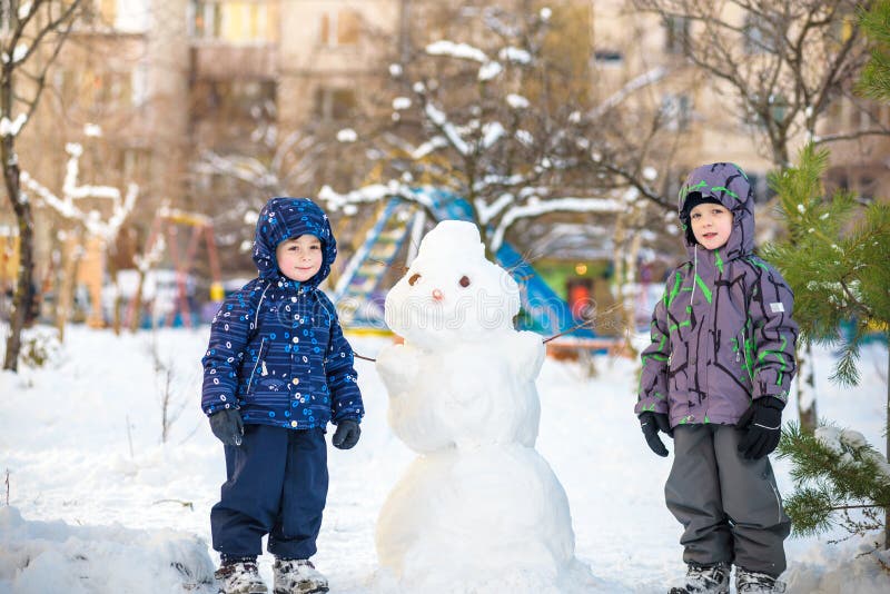 Download Two Little Siblings Kids Boys Making A Snowman, Playing And Having Fun With Snow, Outdoors On ...