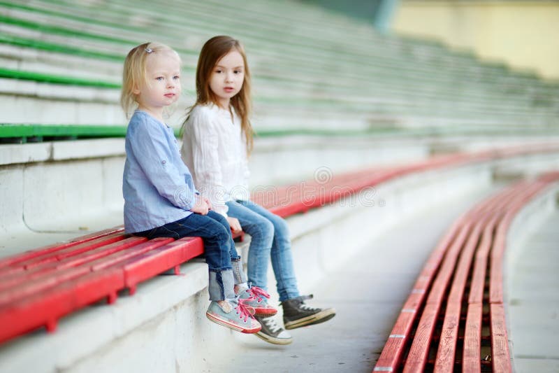 Two little sisters sitting on a stadium seats