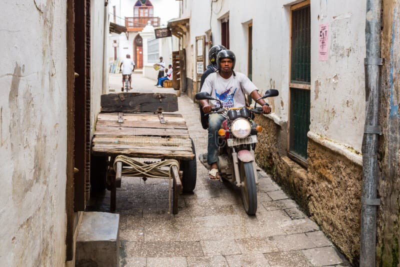 Two local men driving a motorcycle through narrow streets of Stone Town, old colonial center of Zanzibar City, Unguja, Tanzania. royalty free stock image Two local men driving a motorcycle through narrow streets of Stone Town, old colonial center of Zanzibar City, Unguja, Tanzania. royalty free stock image