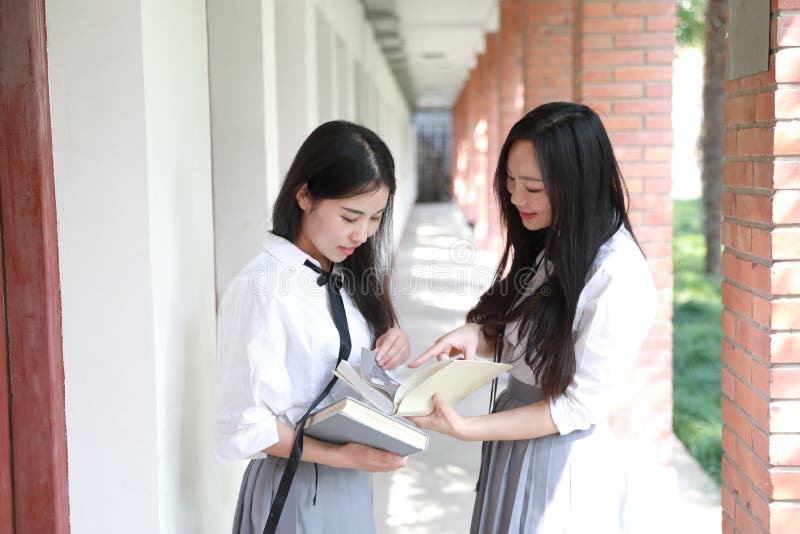 Two lovely Asian Chinese pretty girls wear student suit in school best friends smile laugh reading book in nature