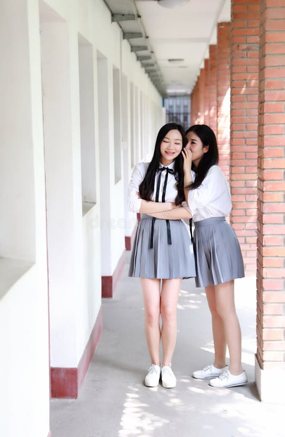 Two lovely Asian Chinese pretty girls wear student suit in school best friends smile laugh talking and gossip