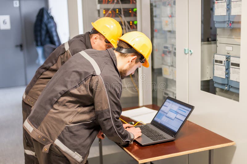 Two maintenance engineers inspect relay protection system with laptop computer. Bay control unit. Medium voltage switchgear