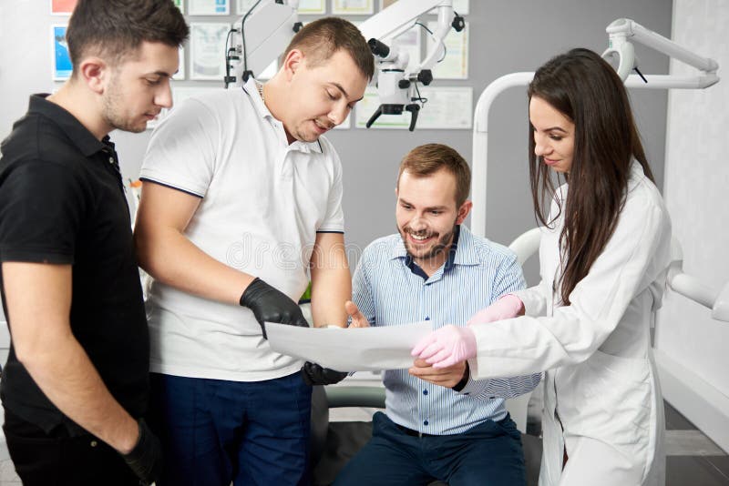 Two male dentists and their female assistant are showing the paper to a satisfied male client of the dental office royalty free stock photo Two male dentists and their female assistant are showing the paper to a satisfied male client of the dental office royalty free stock photo