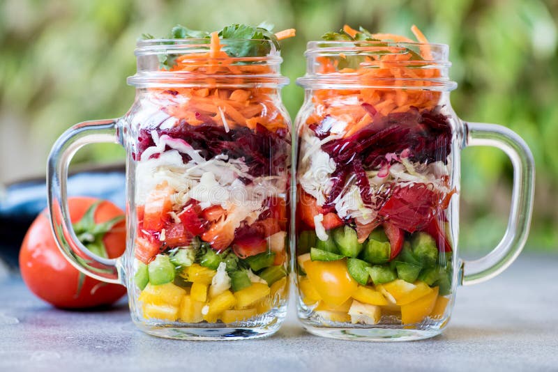 Two mason jars packed with colourful layered fresh vegetable salad to bring to work. Two mason jars packed with colourful layered fresh vegetable salad to bring to work