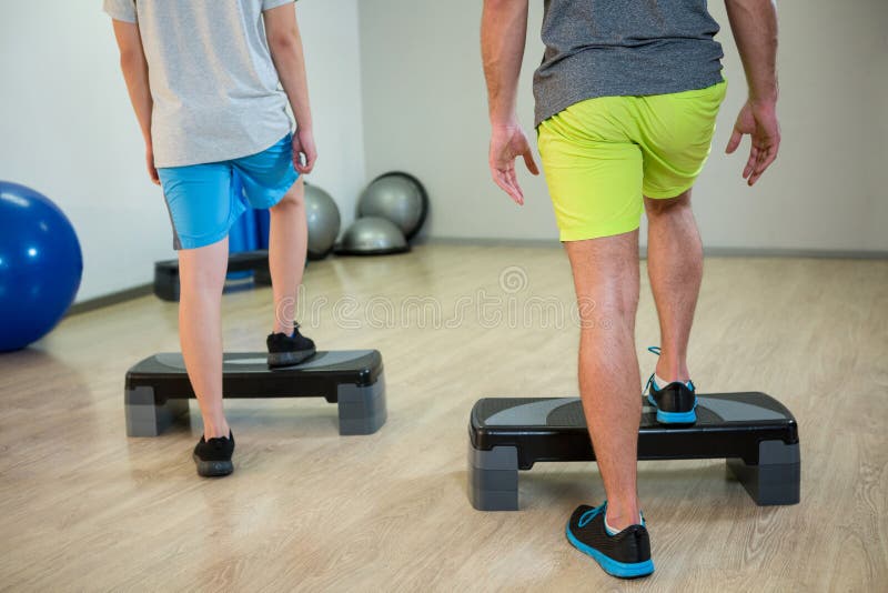 Two Men Doing Step Aerobic Exercise with Dumbbell on Stepper Stock