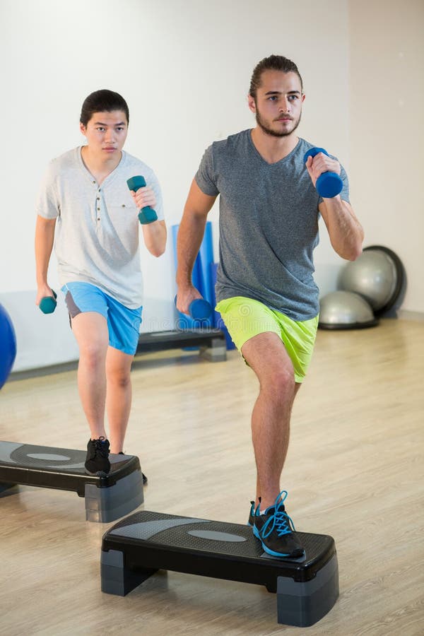 Two Men Doing Step Aerobic Exercise with Dumbbell on Stepper Stock