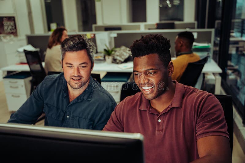 Two mixed race business men working on collaboration project typing on desktop computer in office block stock images