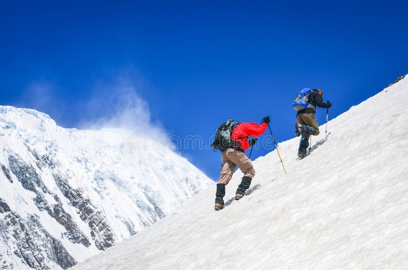 Two mountain backpackers walking on steep hill with snowed peaks background, Himalayas, Nepal