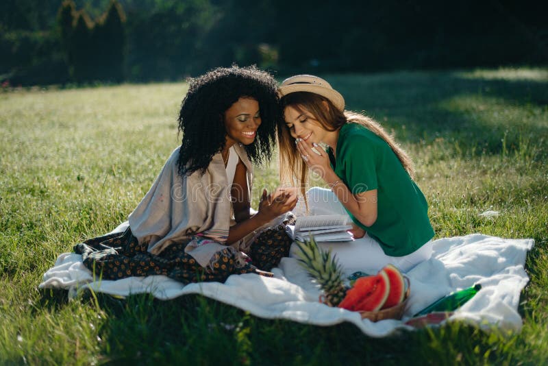 Two multi-ethnic girls are having fun on the picnic. The charming young african girl is showing sonething funny on her