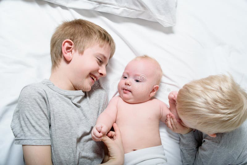 Two Older Brothers Play and Laugh with the Youngest Baby in a White Bed ...