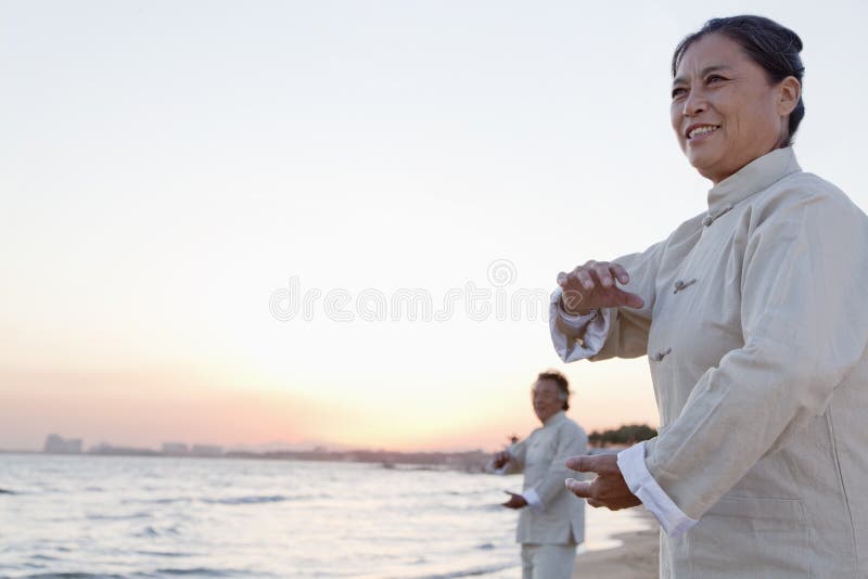 Two older people practicing Taijiquan on the beach at sunset, China