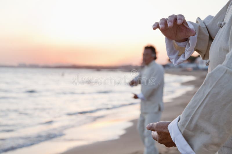 Two older people practicing Taijiquan on the beach at sunset, close up on hands