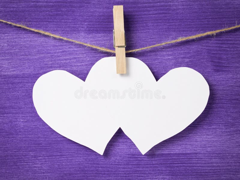 Two paper hearts hanging on rope, purple wooden background