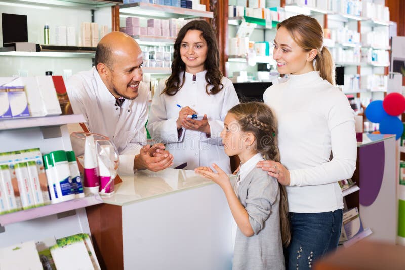 Two cheerful positive pharmacists helping a women and a girl in the pharmacy. Two cheerful positive pharmacists helping a women and a girl in the pharmacy