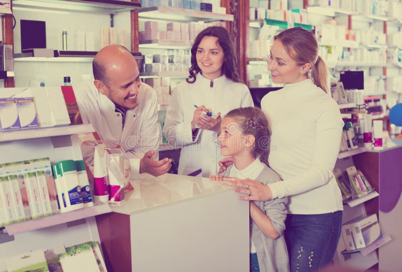 Two cheerful smiling pharmacists helping a women and a girl in the pharmacy. Two cheerful smiling pharmacists helping a women and a girl in the pharmacy