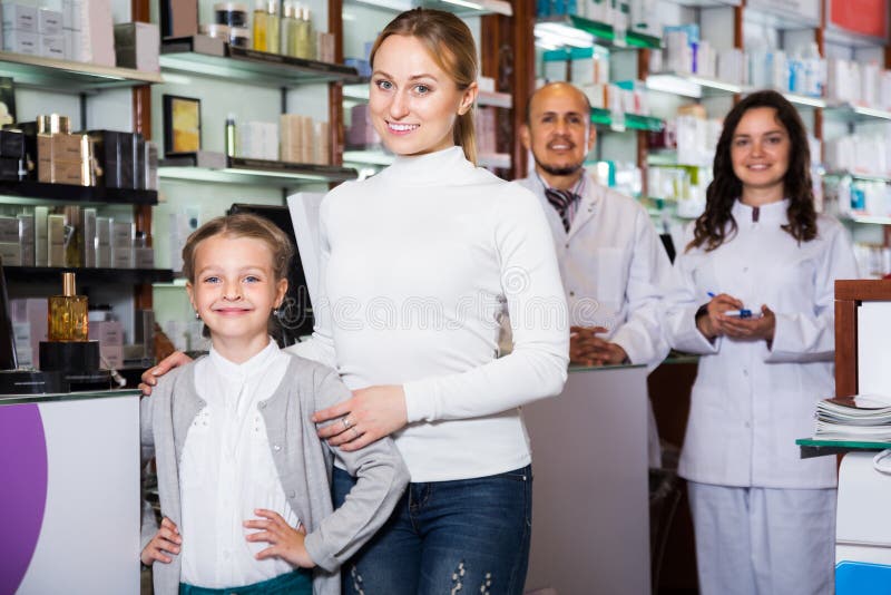 Two cheerful pharmacists helping a women and a girl in the pharmacy. Two cheerful pharmacists helping a women and a girl in the pharmacy
