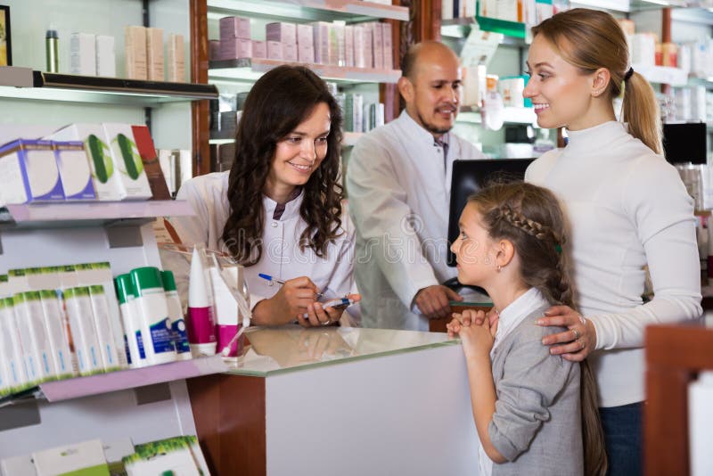 Two pharmacists helping a women and a girl in the pharmacy. Two pharmacists helping a women and a girl in the pharmacy