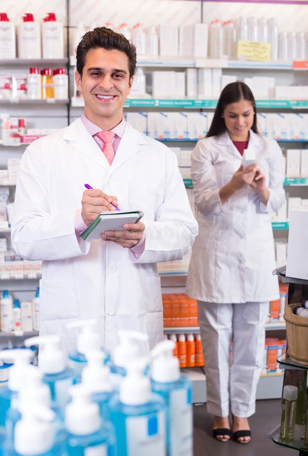 Two smiling professional pharmacists in white uniform at the work in modern pharmacy. Two smiling professional pharmacists in white uniform at the work in modern pharmacy