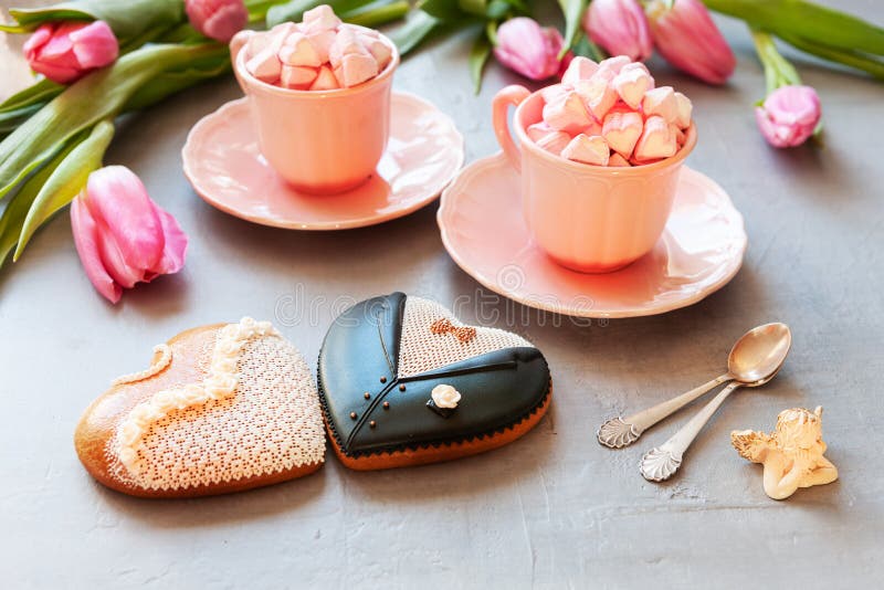 Two pink cups with pink heart shaped marshmallows, pink tulips, angel figurine and two gingerbreads bride and groom form. stock photos Two pink cups with pink heart shaped marshmallows, pink tulips, angel figurine and two gingerbreads bride and groom form. stock photos
