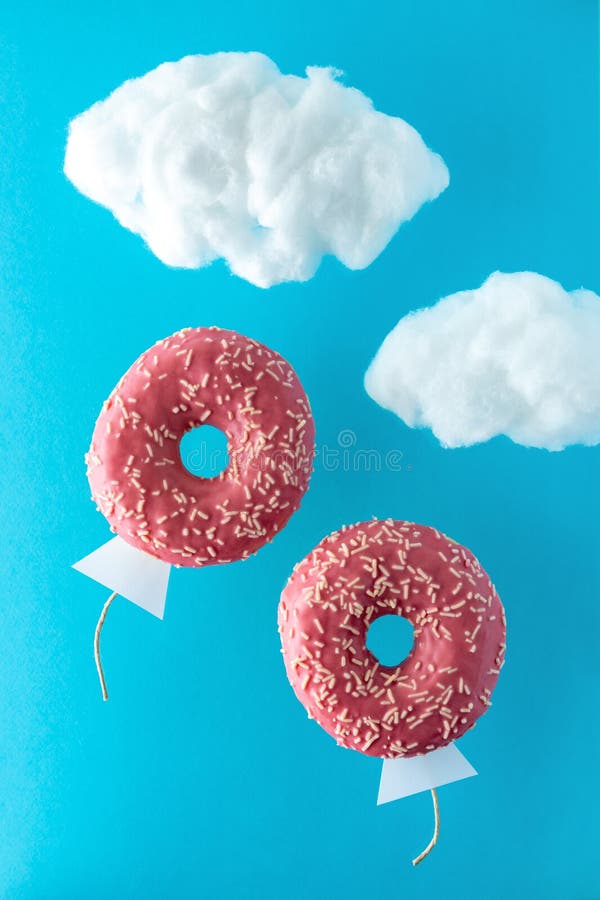 Two pink donuts flying on sky background with fluffy cotton clouds. Minimal concept