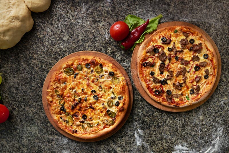 Two pizzas are stone table on kitchen top view