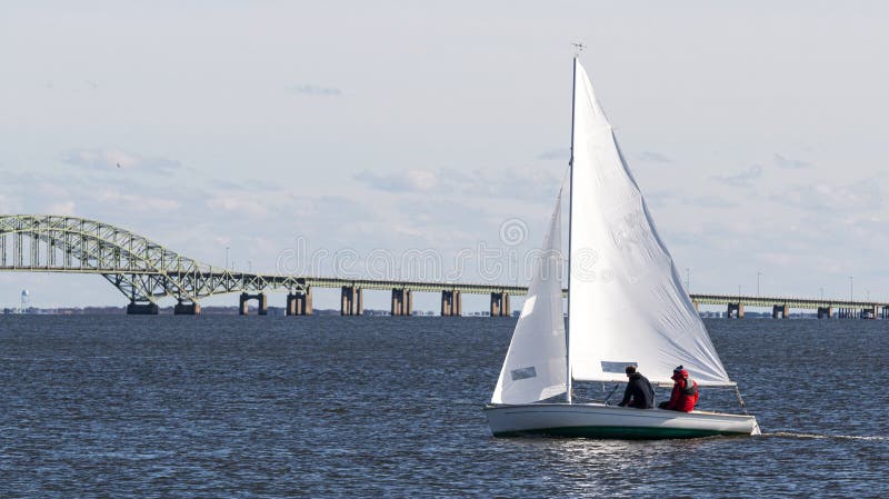 Two poeple on a small sailboat in the winter with the great south bay bridge in background royalty free stock image Two poeple on a small sailboat in the winter with the great south bay bridge in background royalty free stock image
