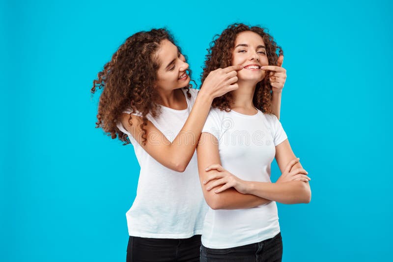 Two Pretty Girls Twins Smiling Showing Okay Over Blue Background