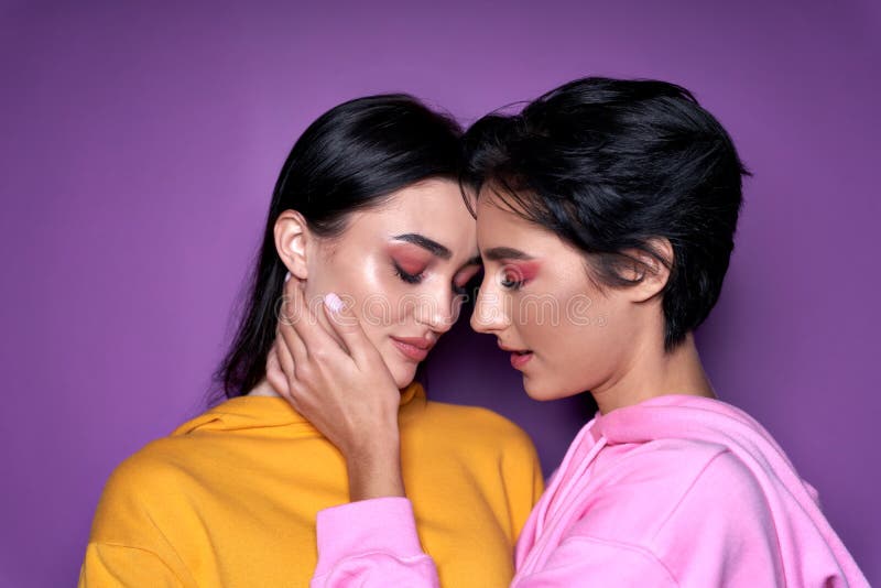 Two cool gen z girls lesbian couple getting closer to kiss on purple background.