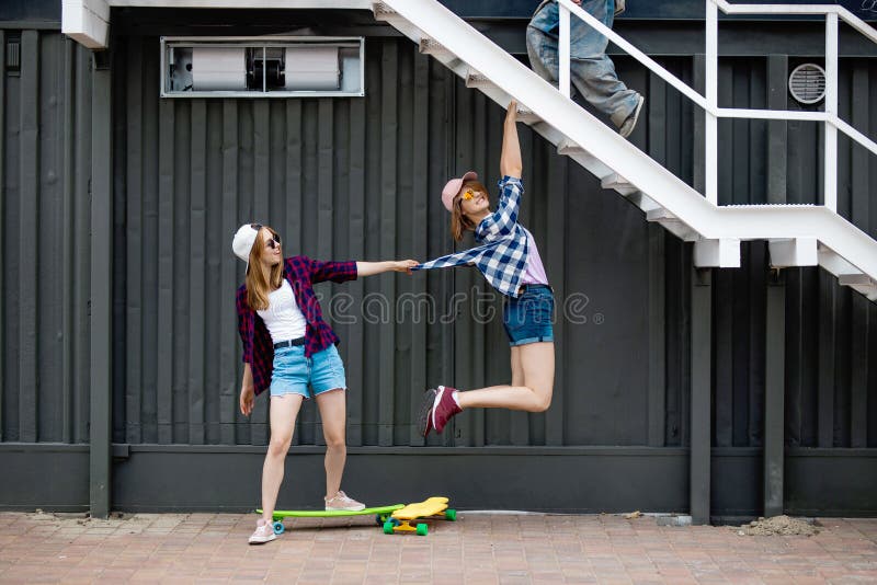 Two pretty smiling blond girls wearing checkered shirts, caps and denim shorts are balancing in front of the black wall stock photos Two pretty smiling blond girls wearing checkered shirts, caps and denim shorts are balancing in front of the black wall stock photos