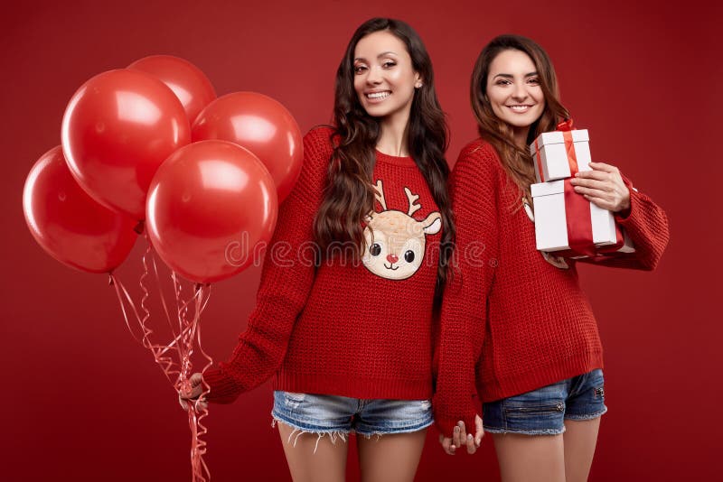 Two pretty twins in winter sweater with party balloons and gift boxes