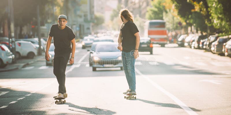 Two pro skateboard rider ride skate through cars on street stock photograph...