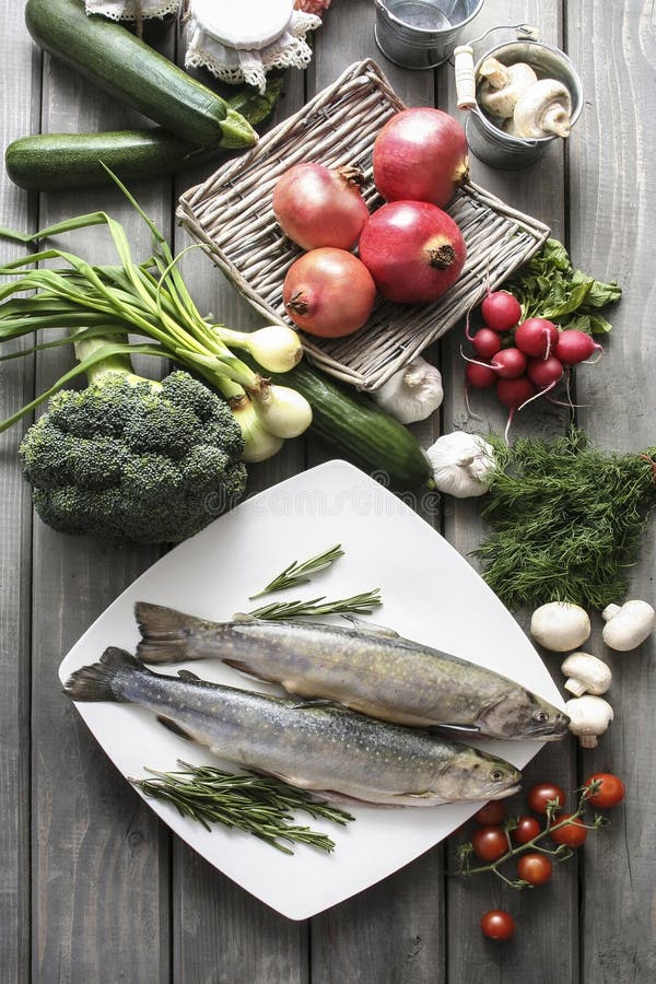 Two raw, fresh rainbow trouts among vegetables.