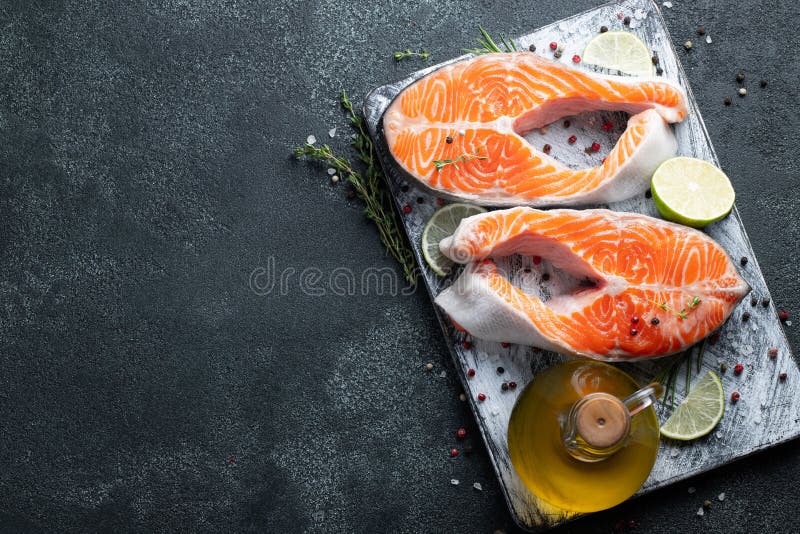 Two raw fresh salmon or trout steaks, rich in omega-3 oil, with lime, thyme and olive oil on a dark background. Healthy and dietary food. Top view with copy space. Flat lay