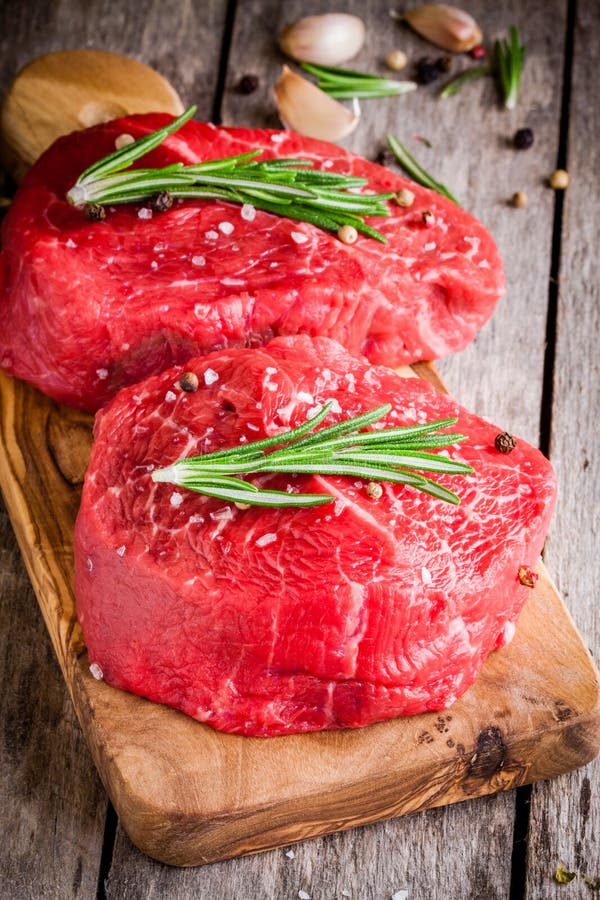 Two raw steaks with rosemary, garlic, salt and pepper