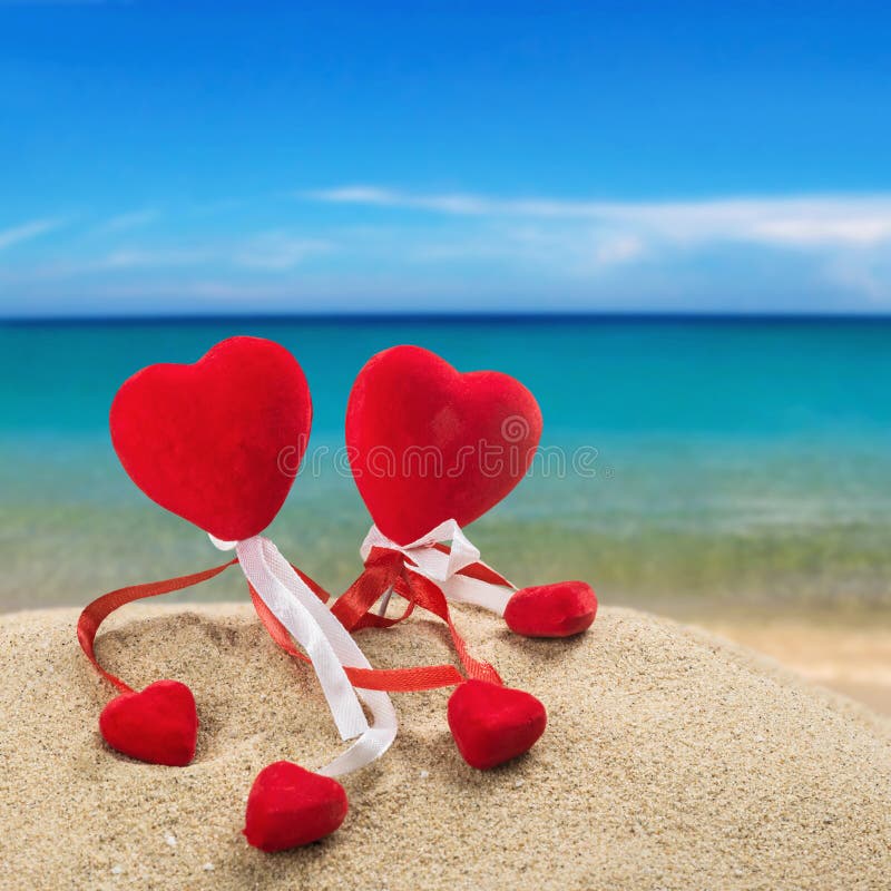 Two red hearts in the sand on the ocean background