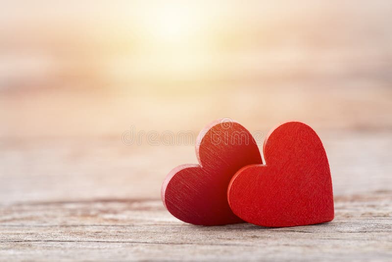 Two red hearts on wooden background in sunset