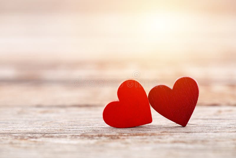 Two red hearts on wooden background in sunset