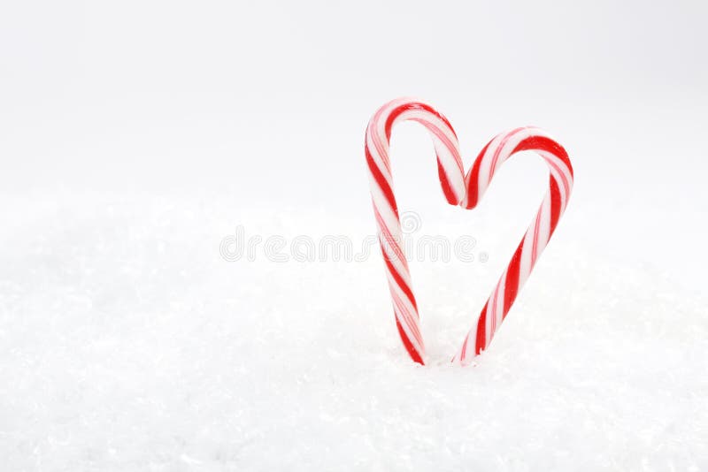 Two red and white candy canes in heart shape on snow