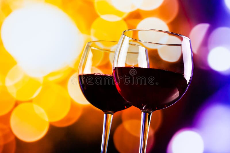 Two red wine glasses against colorful bokeh lights background
