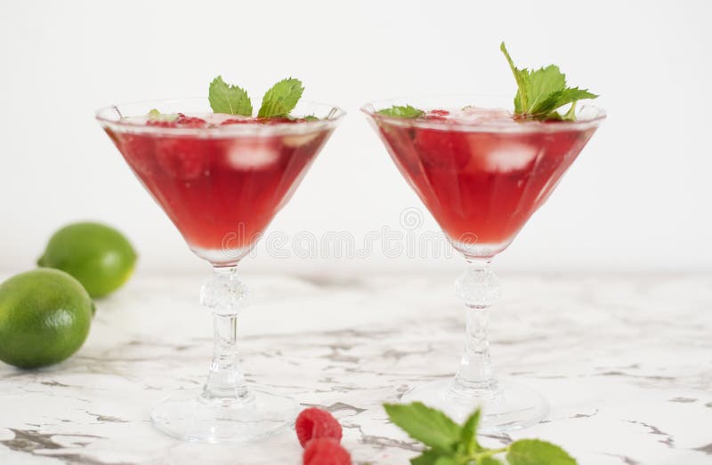 Two refreshing red translucent drinks with ice and raspberries. The raspberry juice is garnished with a green leaf, and there are royalty free stock photo Two refreshing red translucent drinks with ice and raspberries. The raspberry juice is garnished with a green leaf, and there are royalty free stock photo