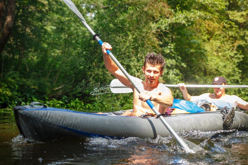 Two rowers in boat with oars in hands on the river on summer day. Young sports guys swim a canoe along the river