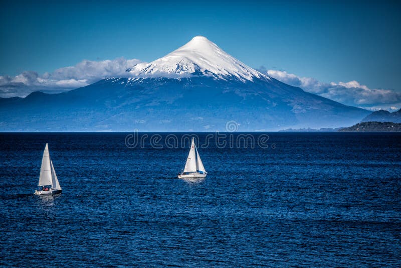 Two sailboats sail in front of snow capped Orsono Volcano in Chile