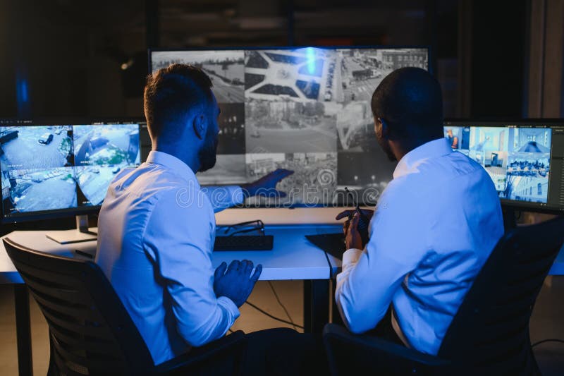 Two security guards sitting by workplace in front of monitors and observing cctv video royalty free stock photography