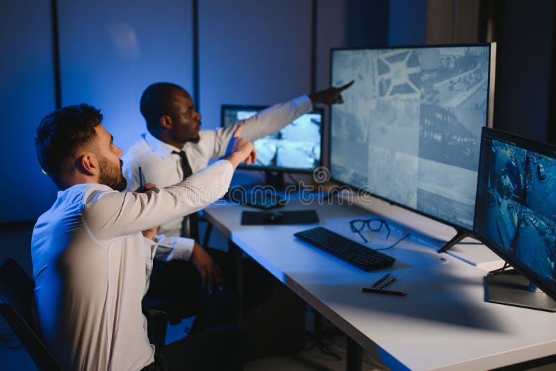 Two security guards sitting by workplace in front of monitors and observing cctv video stock photography