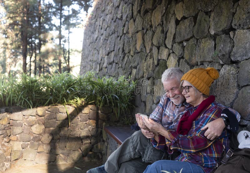 Two senior people resting on a sheltered bench after the hike in the mountains. Background of stones and forest. They look